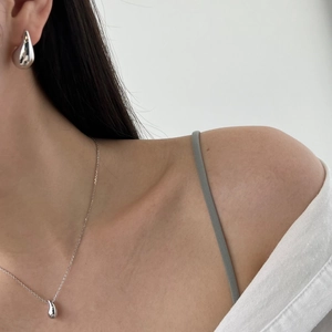 Close-up of minimalist silver teardrop pendant necklace and stud earrings worn by a model
