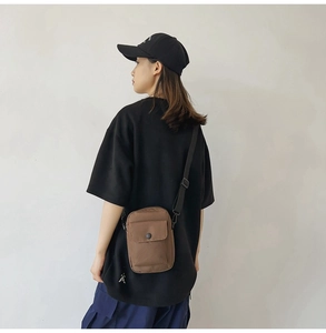 Brown canvas crossbody bag shown on model's back with adjustable strap and snap flap