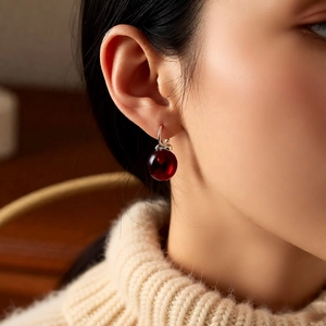 Close-up of deep red apple pendant earrings on model with a soft knit sweater