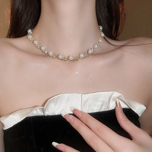 Dettaglio della collana girocollo dorata con perle bianche e strass scintillanti
