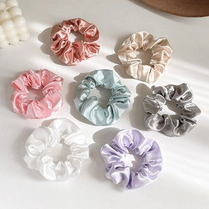 Elegantes Set aus Satin-Haargummis in sieben Pastellfarben auf schlichtem Hintergrund