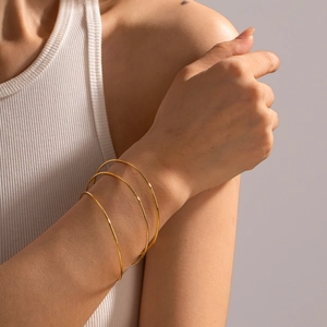 Minimalist gold titanium steel bangles shown as a stacked three-piece set on a model