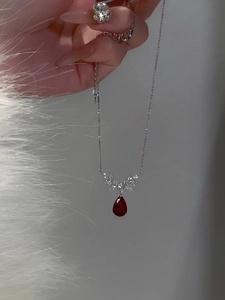 Macro shot of silver wing-shaped pendant with red teardrop zircon on a fine chain