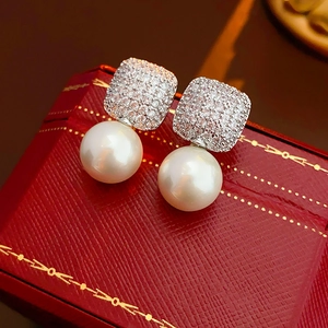 Macro shot of silver zircon square stud earrings with white pearls on a red box