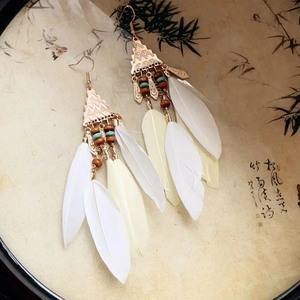 Detail of bohemian long feather earrings with gold geometric accents and wooden beads
