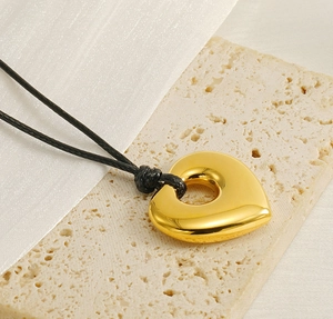 Detail of a polished gold heart pendant on a black wax rope over a stone background