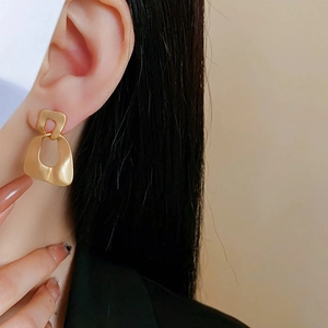 Close-up of minimalist matte gold geometric drop earrings worn by a model in profile