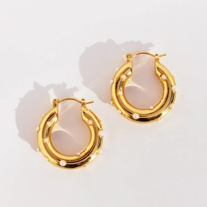 Elegant gold hoop earrings with white pearl inlay set on a minimalist cream background