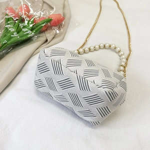 Detail view of woven shell bag with elegant pearl handle and gold chain strap on white fabric