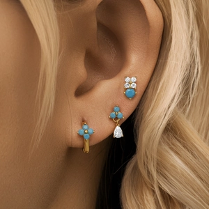 Detail shot of turquoise four-pointed star earring set and gold studs on ear model