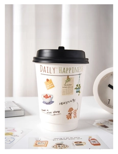 Detail of DAILY HAPPINESS decorative cup with stickers on a desk with laptop and clock