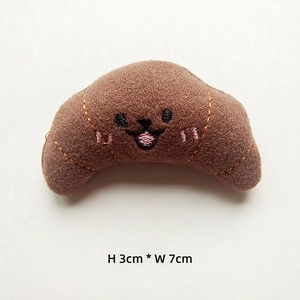 Mini plush croissant charm accessory featuring a 7cm x 3cm soft fabric smiling face design