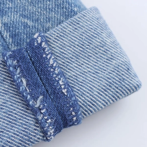 Gros plan des coutures contrastées et de l'ourlet roulé sur texture denim bleu