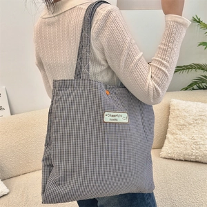 Close-up of black and white checkered canvas tote bag with a green Cheerful label