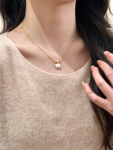 Détail du collier pendentif étoile en perle dorée porté par un mannequin pour un look chic