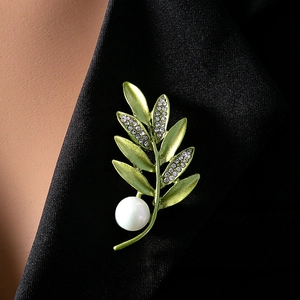 Macro view of olive branch brooch with green enamel leaves and white pearl on black suit