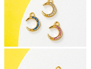 Detailed shot of three gold moon charms with blue, pink, and clear gems on yellow background