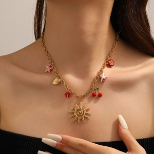 Gros plan détaillé du collier en acier doré avec pendentifs soleil, cerise et étoile de mer