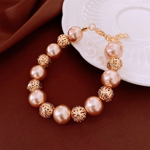 Detailed shot of a gold hollow bead and pearl bracelet on a vintage ceramic plate