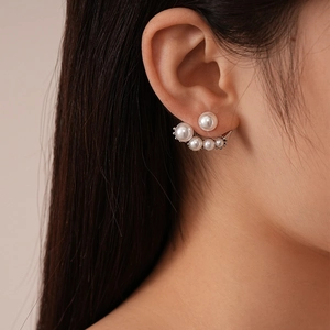 Close-up of elegant ear jacket earrings with white pearls and silver metal setting on model