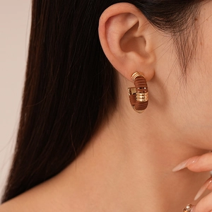Gros plan d'une boucle d'oreille en simili cuir en forme de C portée en tons brun et or