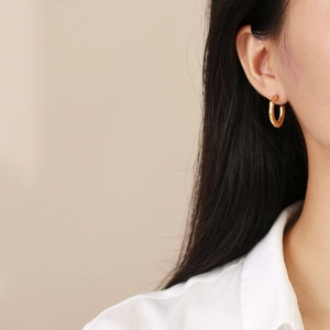 Close-up of chunky gold C-shaped hoop earrings with bamboo texture worn by a model