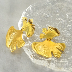 Elegant gold ginkgo leaf stainless steel earrings on a textured glass tray background