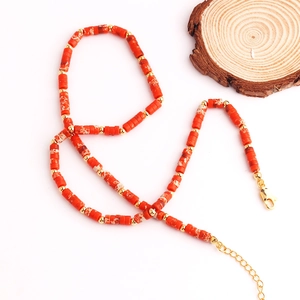 Collar de acero inoxidable bañado en oro con cuentas cilíndricas rojas en fondo blanco