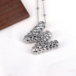 Macro shot of silver letter W pendant with rivet texture on a minimalist necklace