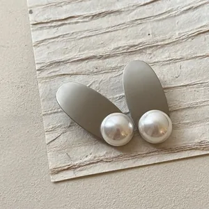 Detail of matte gold alloy clip with elegant large pearl on a cream textured background