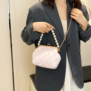 Detail of pink shell bag with large pearl handle and gold chain strap held by a model