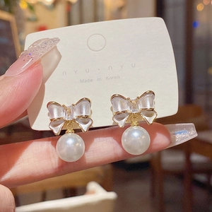 Detailed close-up of bow knot pearl earrings with gold plating on a display card