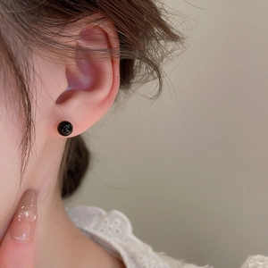 Close-up of a minimalist glossy black spherical stud earring worn on the earlobe