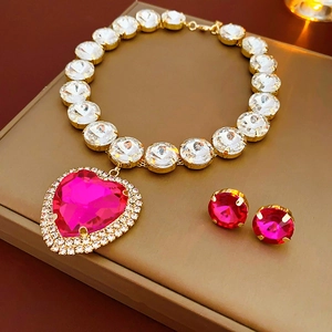 Close-up of gold necklace set featuring a pink heart crystal pendant and matching earrings