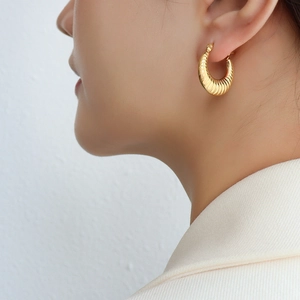 Boucles d'oreilles créoles dorées en acier titane texturé portées par un mannequin