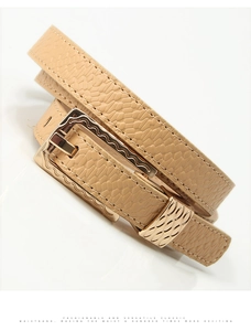 Detail of light beige faux crocodile belt with decorative gold wavy buckle and slim texture