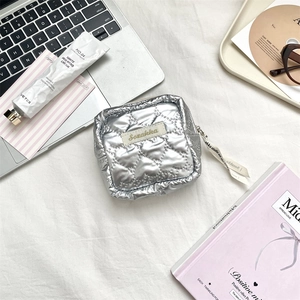 Silver metallic quilted storage pouch with ribbon zipper detail on a minimalist desk