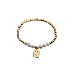 Detailed macro of gold beaded bracelet with pearls and square pendant engraved with letter C