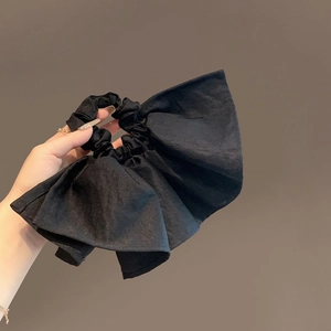 Elegant black oversized bow scrunchie made of textured knit fabric held in hand