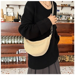 Beige corduroy crescent crossbody bag shown on model in a natural cafe setting