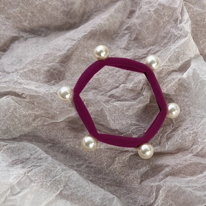 Close-up of dark purple and wine red elastic hair ties with six faux pearls on grey paper