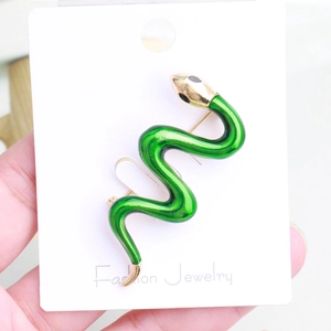Macro detail of a green enamel snake brooch with gold accents on a jewelry display card