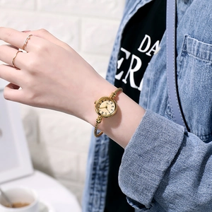 Detail of gold open bangle watch with roman numerals on model's wrist with denim shirt