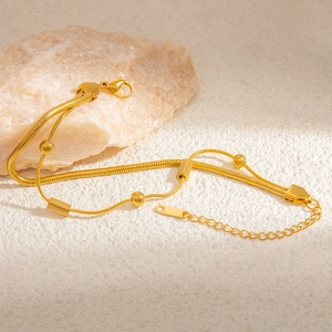 Close-up of dual-layer gold stainless steel snake chain bracelet on a white stone background