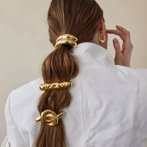 Dettaglio di accessori per capelli dorati in acciaio e orecchini a goccia su modella