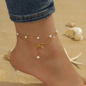 Double-layered gold anklet with pearls and a bow pendant on a beach background