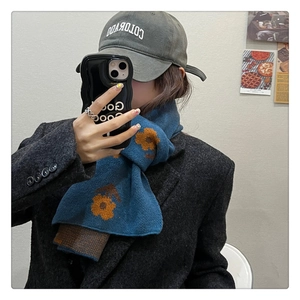 Close-up of knit scarf in lake blue with orange flower pattern and plaid texture