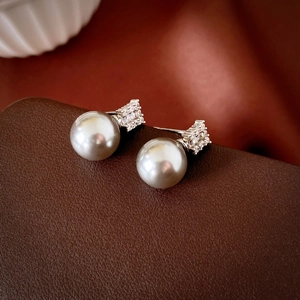 Macro shot of gray pearl earrings with sparkling white cubic zirconia on a leather background