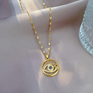 Macro detail of gold-plated evil eye necklace with blue gemstone on pink silk fabric