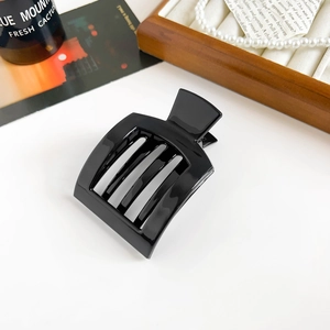 Glossy black square hair claw clip for ponytail displayed on a white desk with jewelry